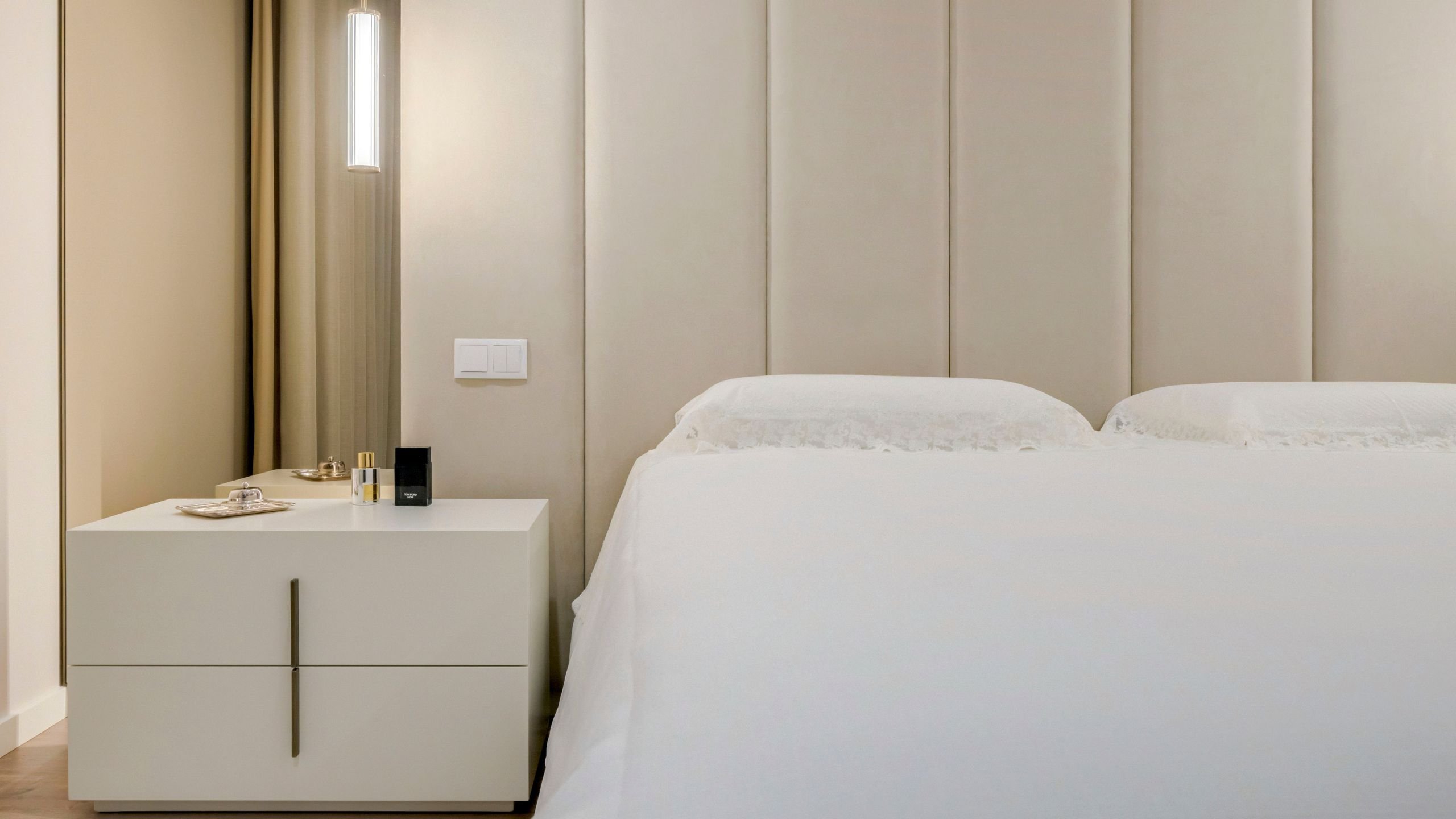 Quarto principal com cabeceira de painéis estofados, mesa de cabeceira Kensington branca e iluminação pendente suave.