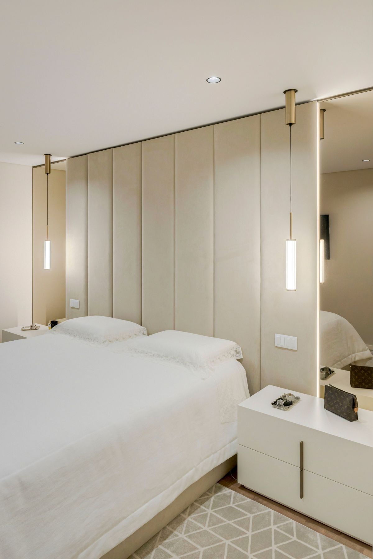 Quarto moderno com cama com sommier, painéis de parede estofados em bege, candeeiros pendentes e mesas de cabeceira Kensington.