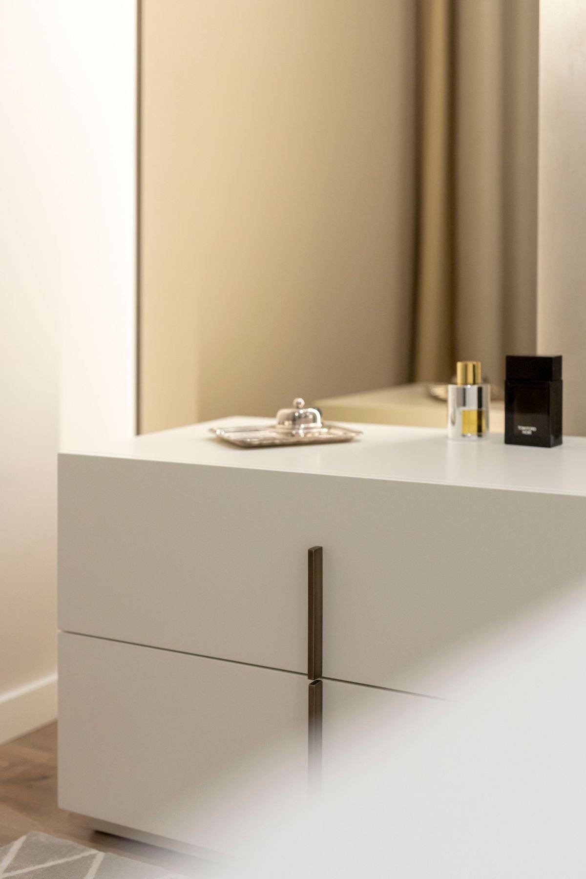 Pormenor de mesa de cabeceira Kensington em branco lacado com frascos de perfume e espelho vertical de fundo.