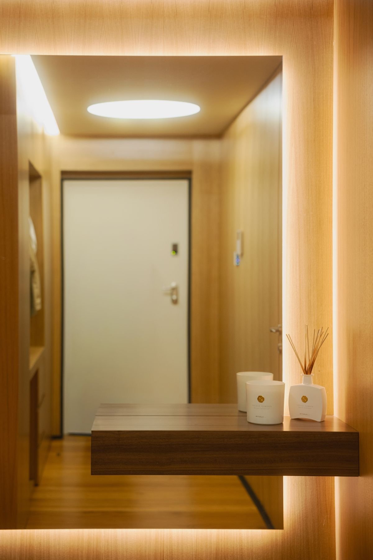Detalhe de consola suspensa em madeira com difusor de aroma e vela decorativa, em frente a espelho com iluminação LED retroiluminada.