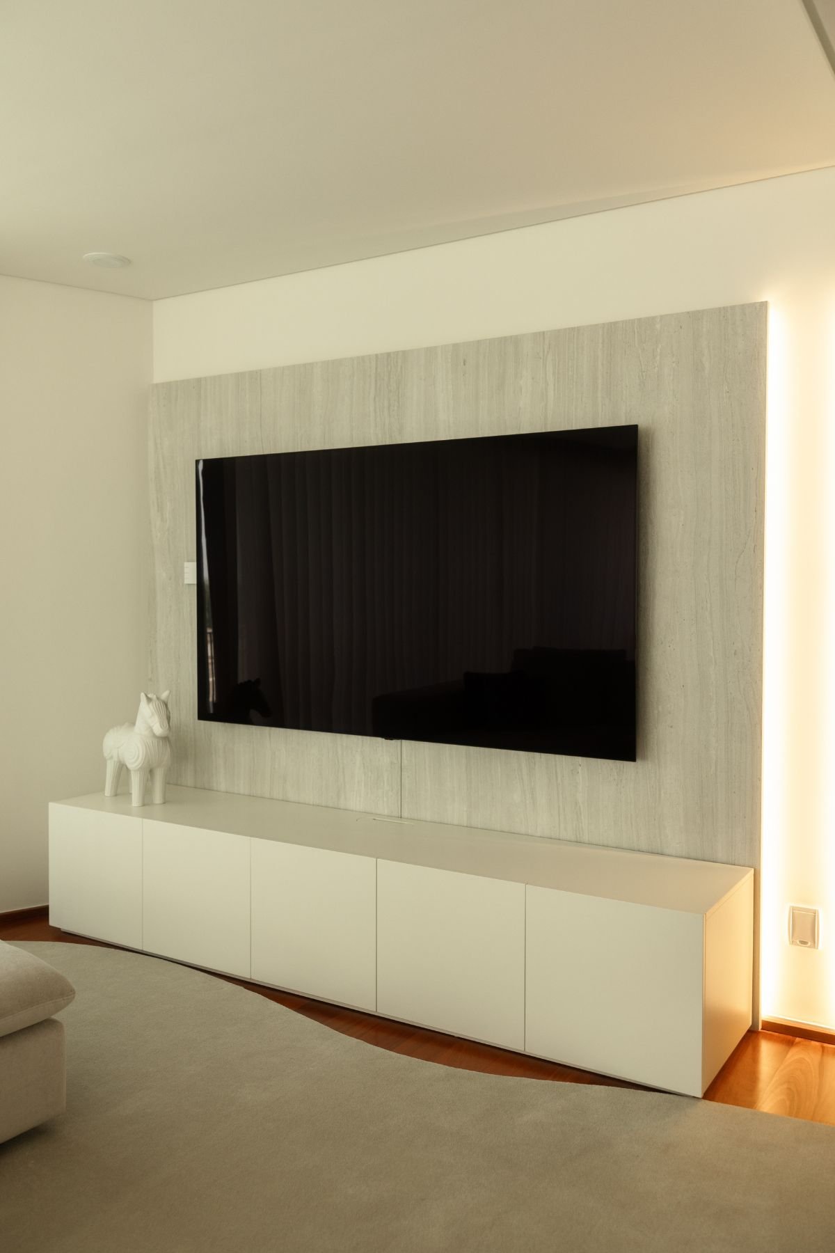 Painel de parede com televisão encastrada, iluminação LED embutida na lateral e móvel de apoio inferior em laqueado branco.