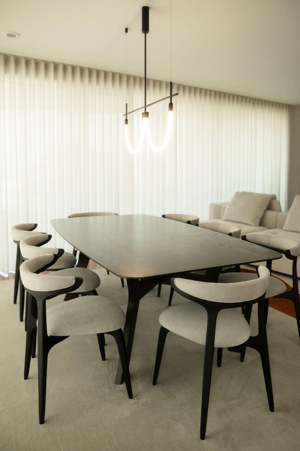 Perspetiva da mesa de jantar para oito pessoas com cadeiras de design contemporâneo e candeeiro suspenso minimalista.