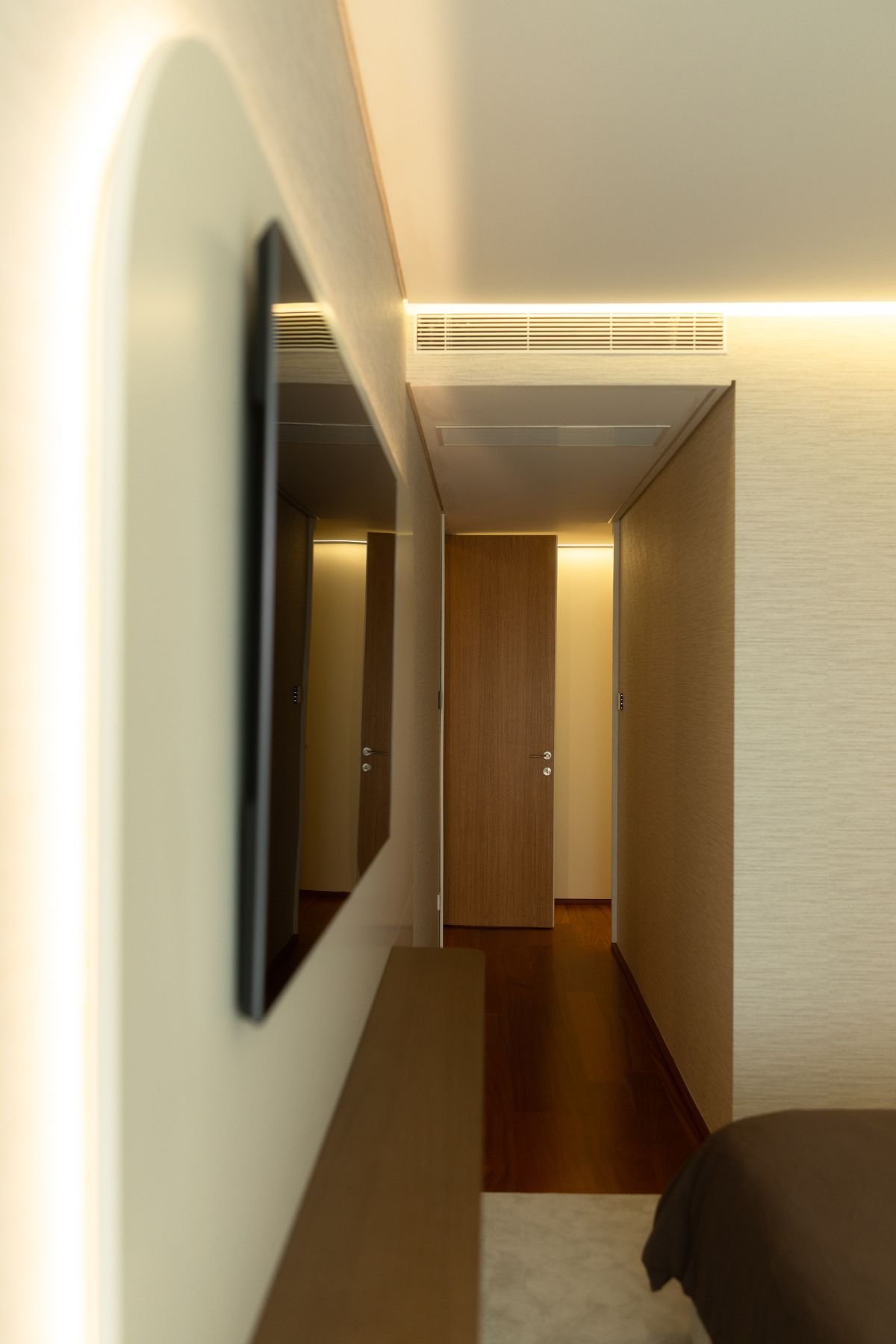 Detalhe de perfil do painel de TV flutuante com retroiluminação LED e estante inferior estreita em madeira.