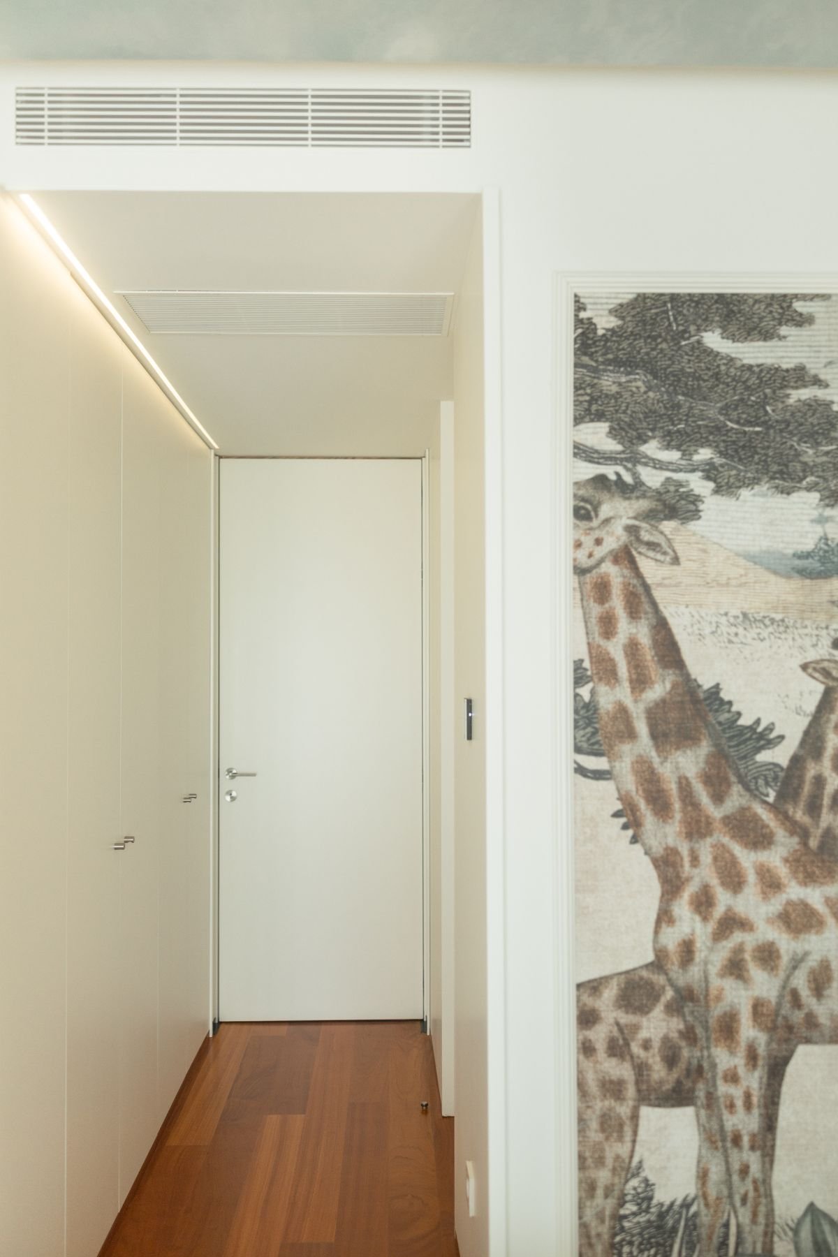 Vista do corredor de acesso ao quarto de criança com roupeiro embutido branco e detalhe de painel decorativo da savana.