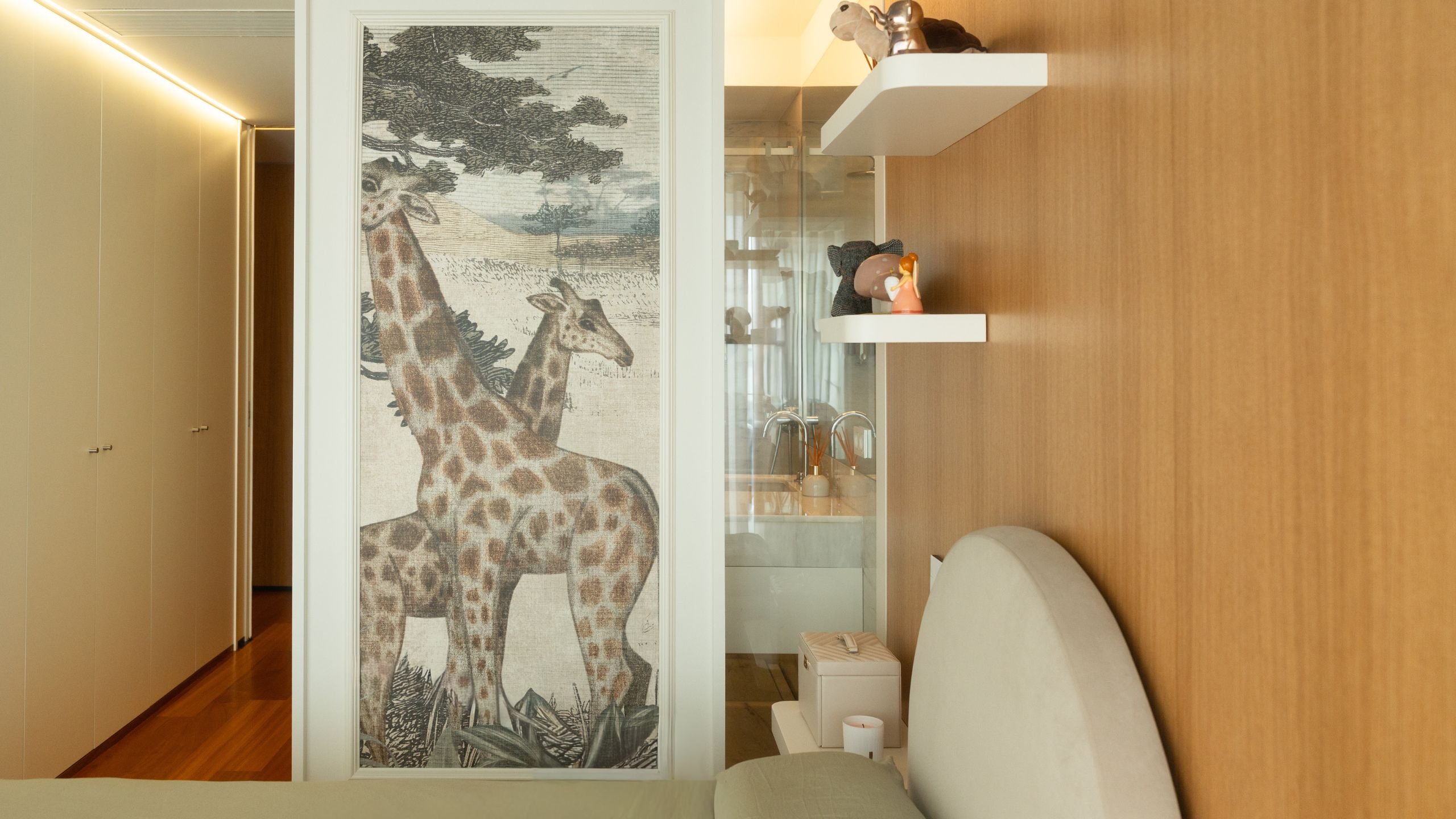 Perspetiva da cama de solteiro com cabeceira redonda, vista para o papel de parede de girafas e entrada para a casa de banho ao fundo.