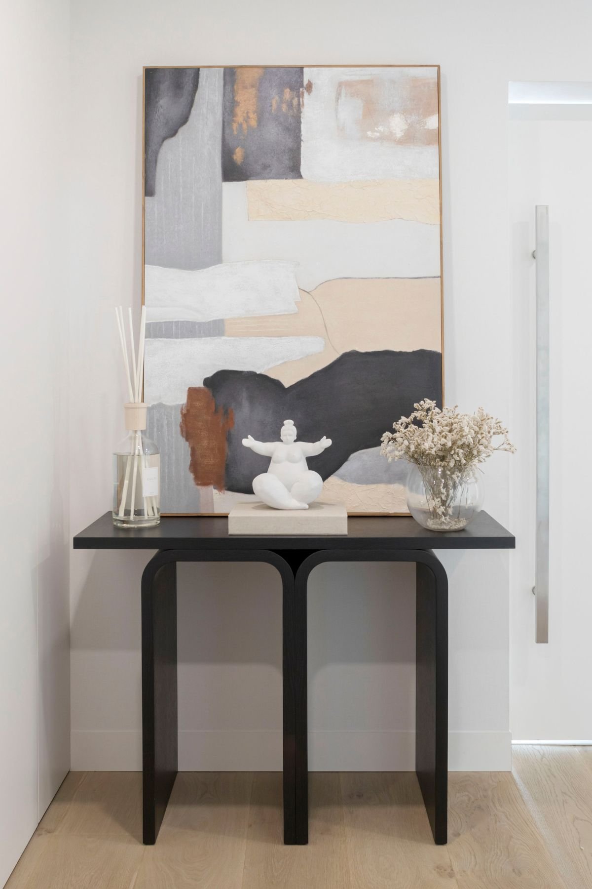 Hall de entrada simples e elegante com consola moderna em tom escuro, quadro abstrato e peças decorativas minimalistas.