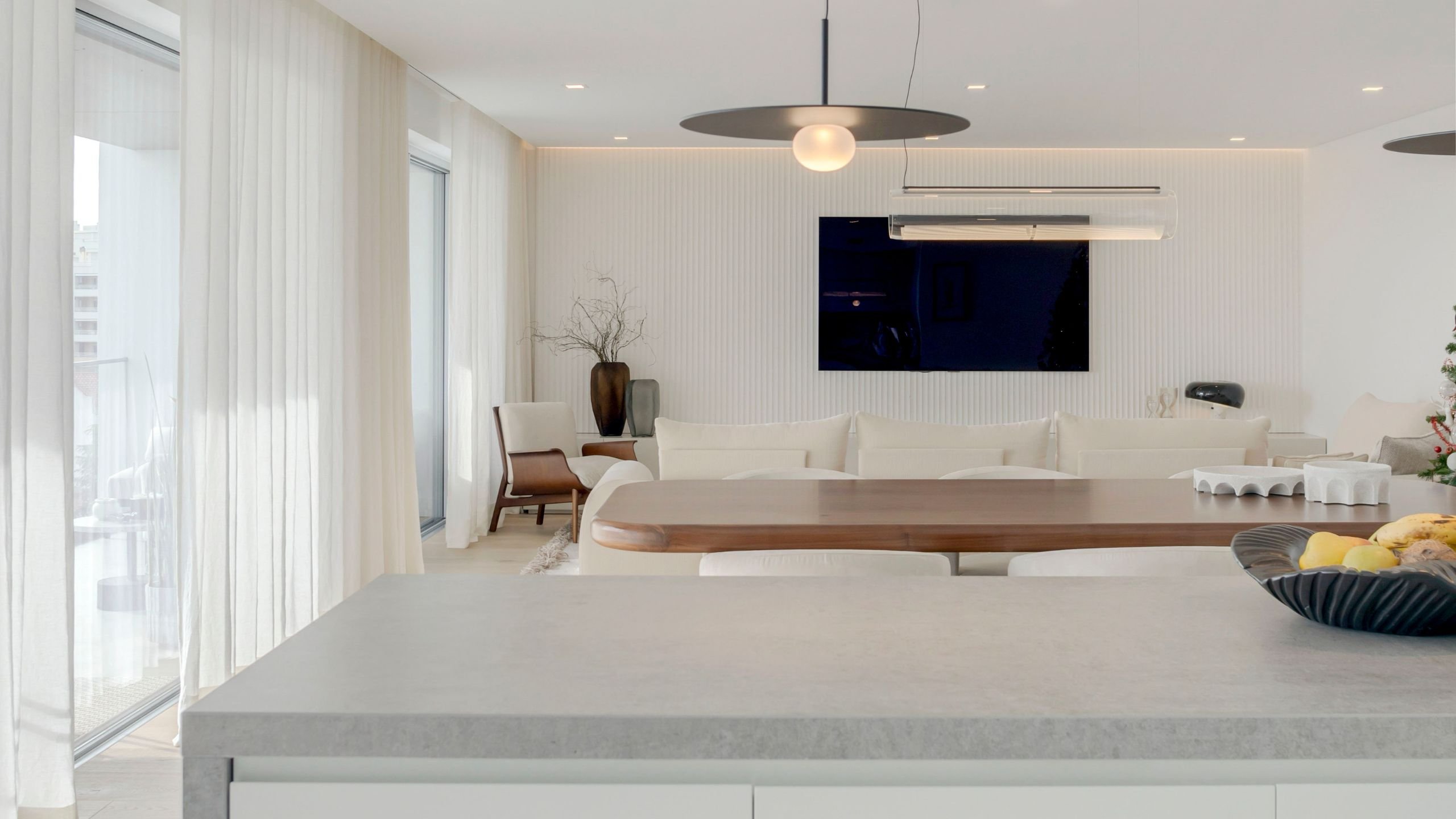 Vista ampla a partir da banca da cozinha em direção à sala de jantar e sala de estar moderna iluminadas por luz natural.