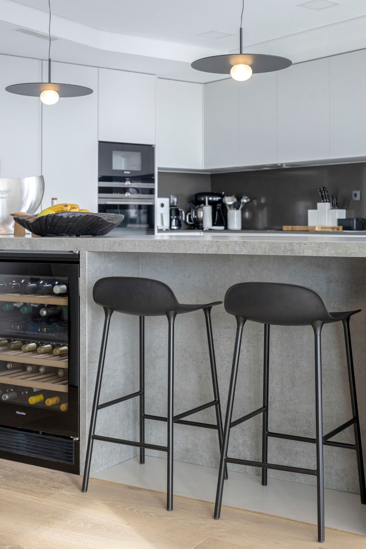 Detalhe da bancada de cozinha com garrafeira de encastrar e dois bancos altos minimalistas.