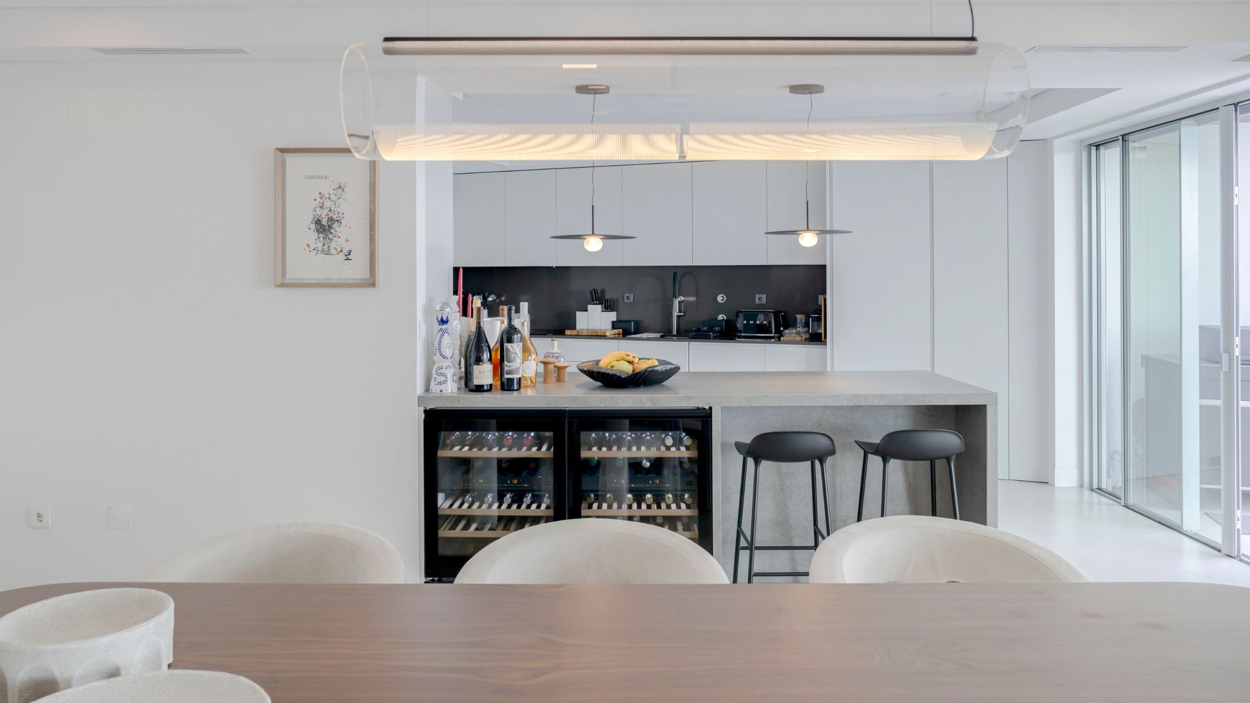 Perspetiva integrada da mesa de jantar em carvalho e da cozinha moderna com ilha e bancos altos.