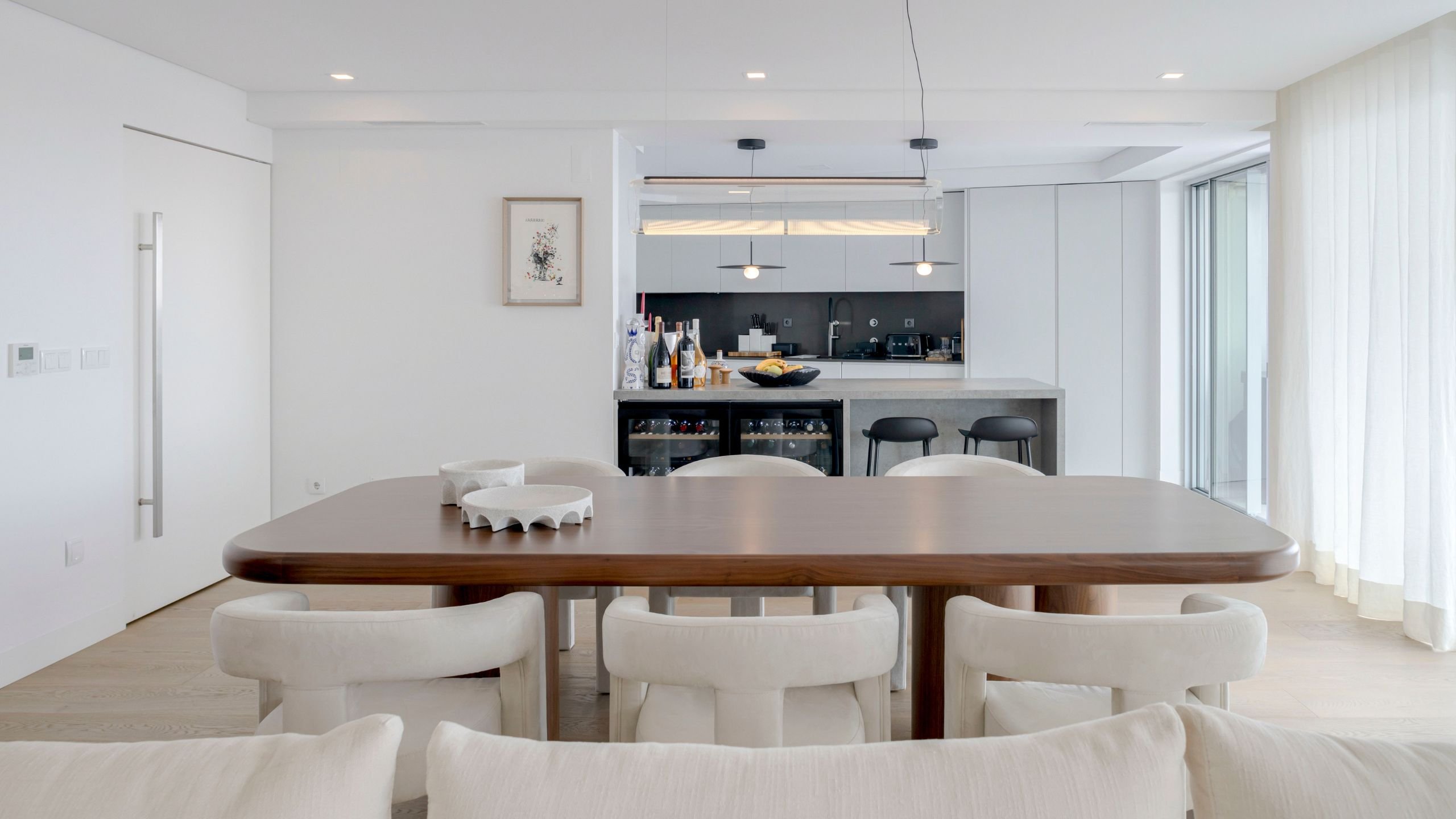 Vista frontal da mesa de jantar e cadeiras estofadas com a cozinha por medida e ilha central em plano de fundo.