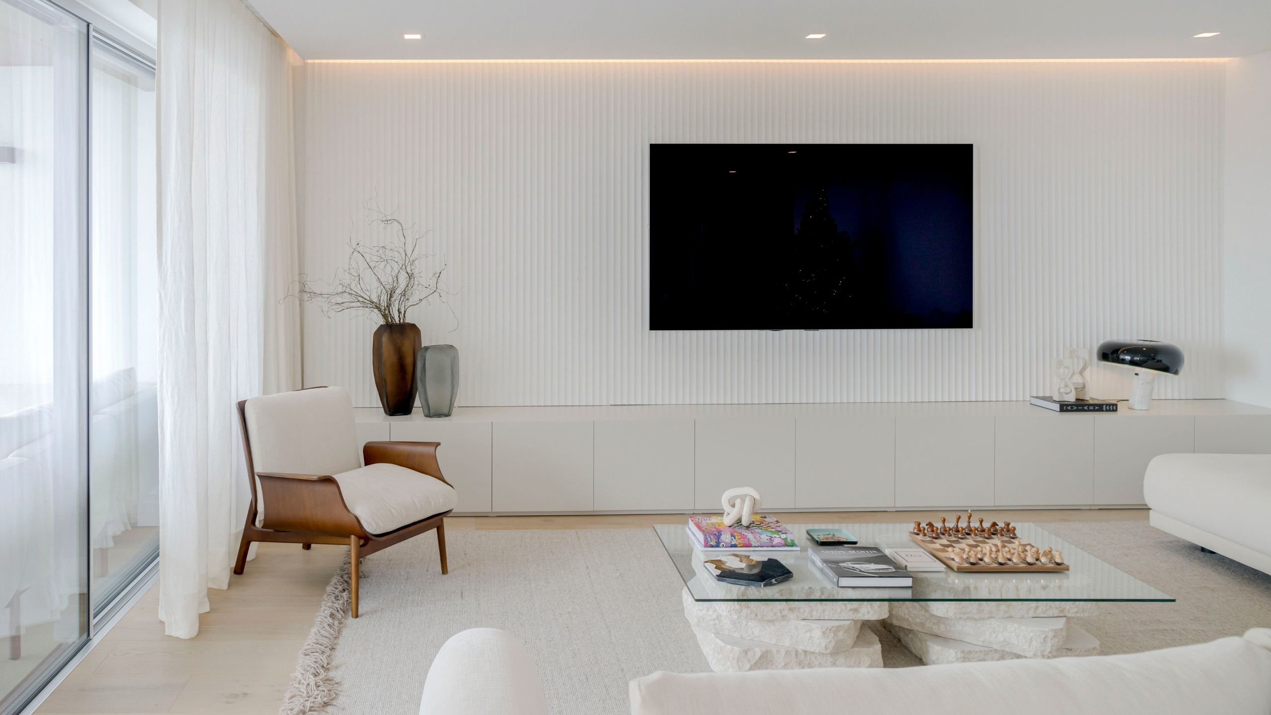 Sala de estar moderna com parede texturizada, destacando móveis sala tv modernos, um cadeirão elegante e uma mesa de centro com tampo de vidro e base em pedra natural.