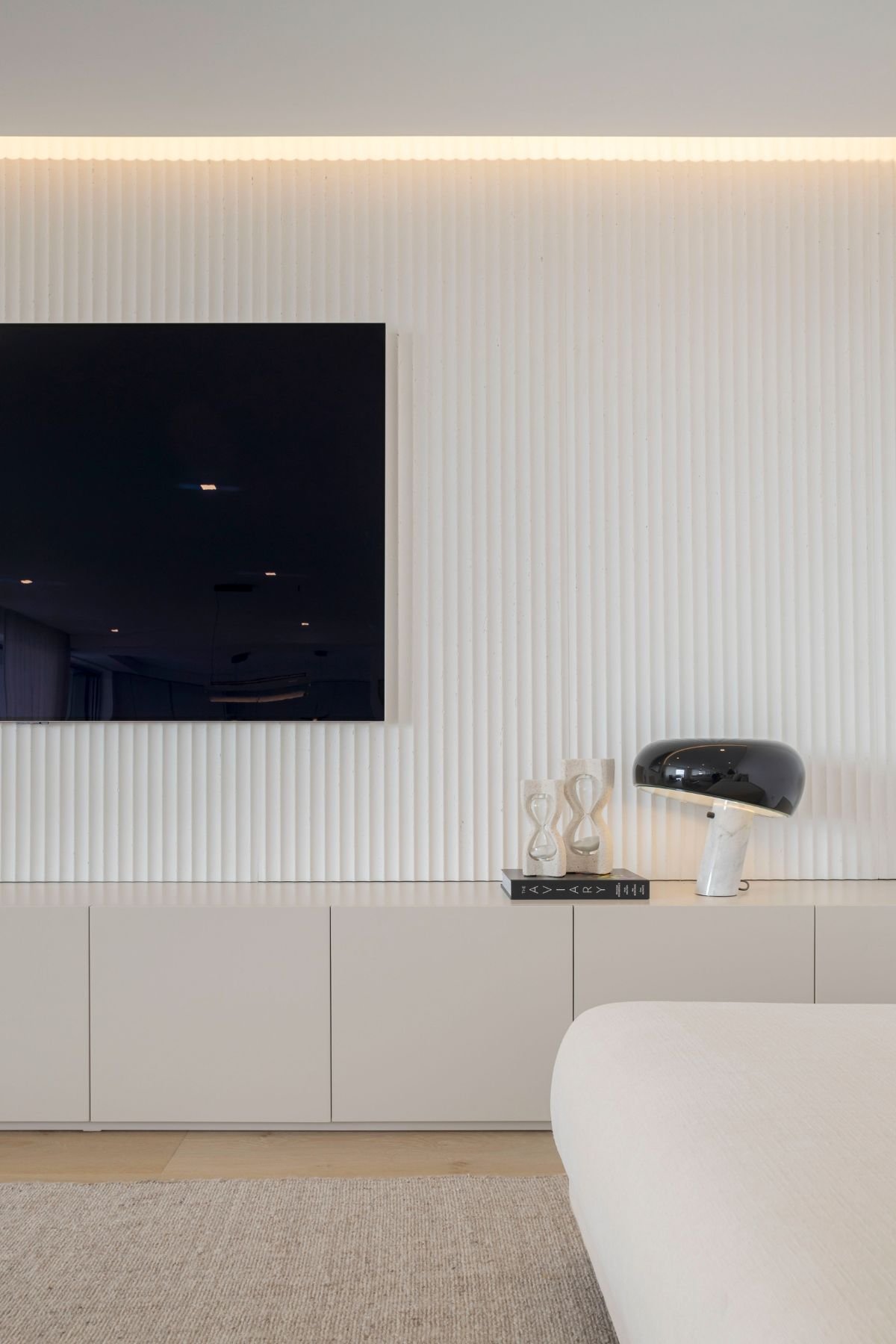 Móvel suspenso de apoio com painel de TV ripado ao fundo, decorado com candeeiro de mesa e objetos concetuais.