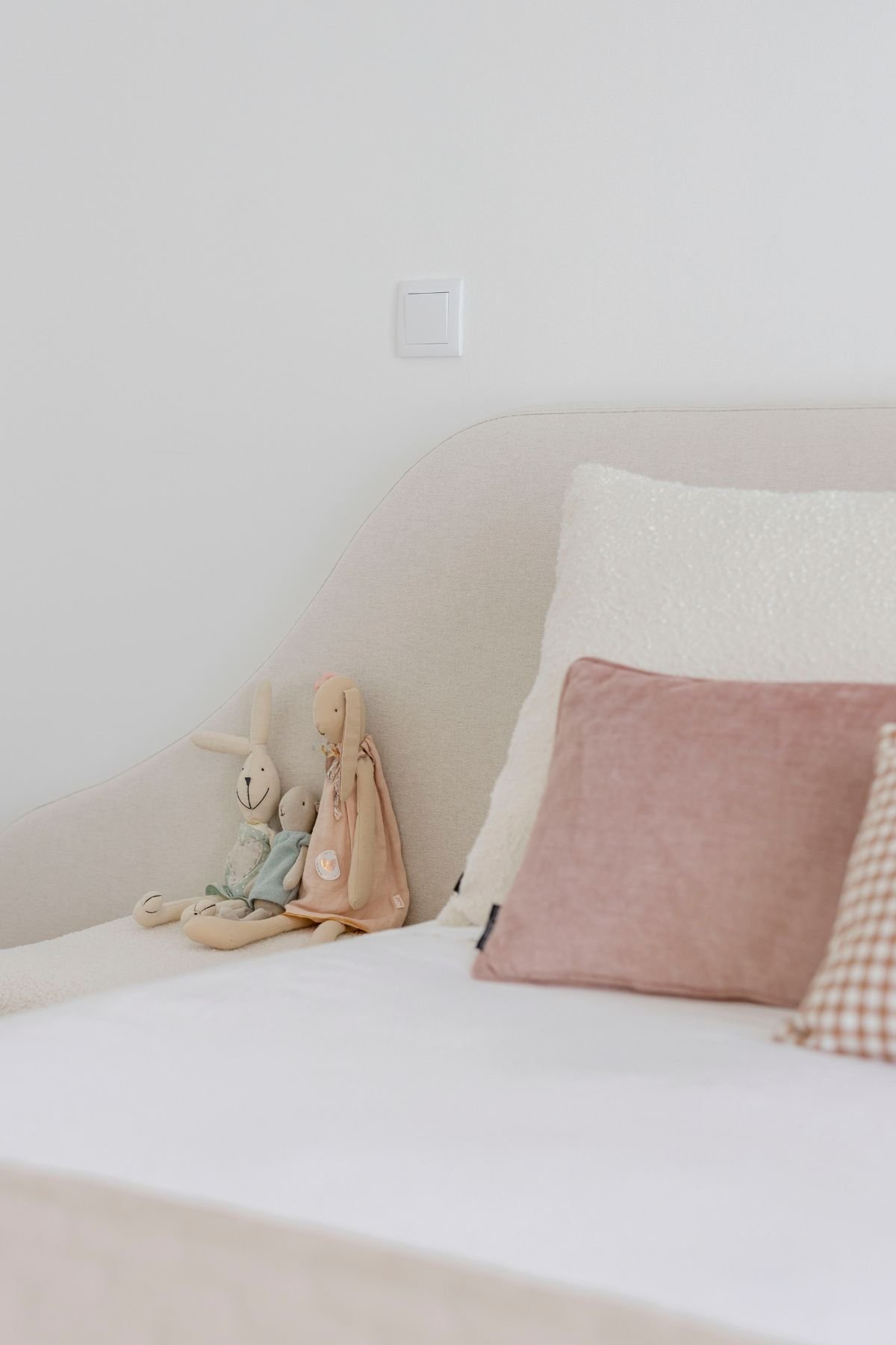 Pormenor dos peluches pousados no pufe bouclé junto à cabeceira da cama.
