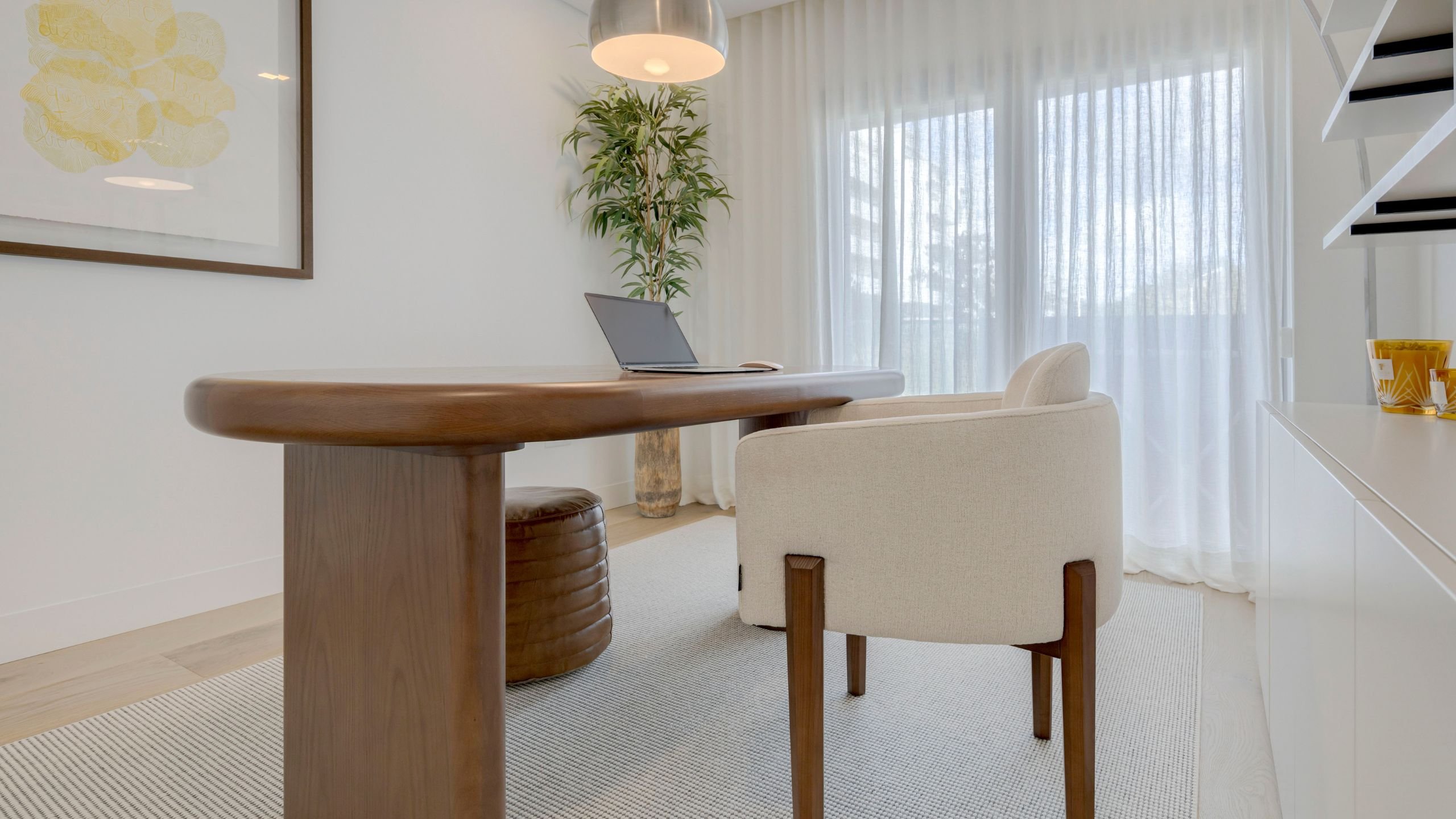 Perspetiva da mesa de trabalho em madeira sobre o tapete claro com pufe em pele de apoio.