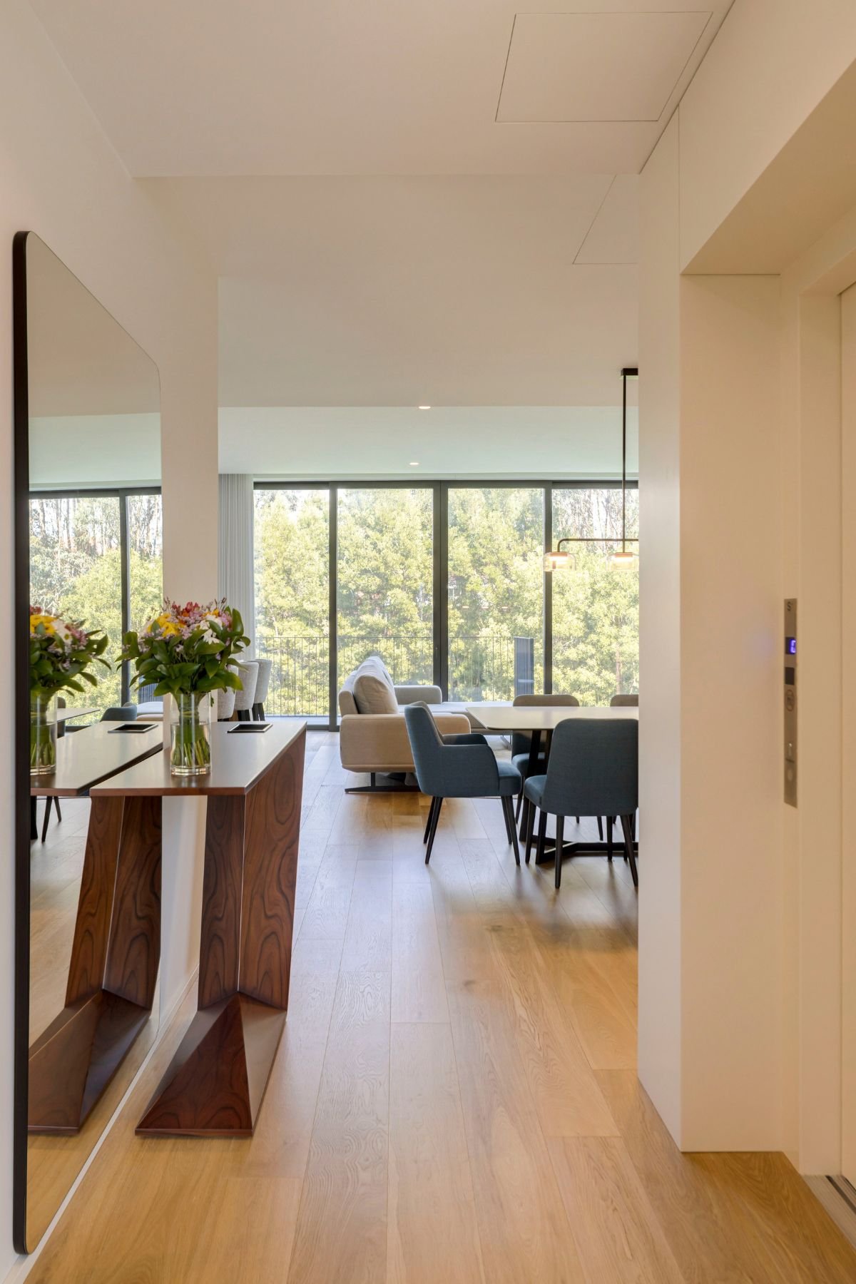 Entrada ampla em open space com vista para a sala. Destaque para a consola entrada em madeira e um espelho grande, numa decoração de interiores minimalista.