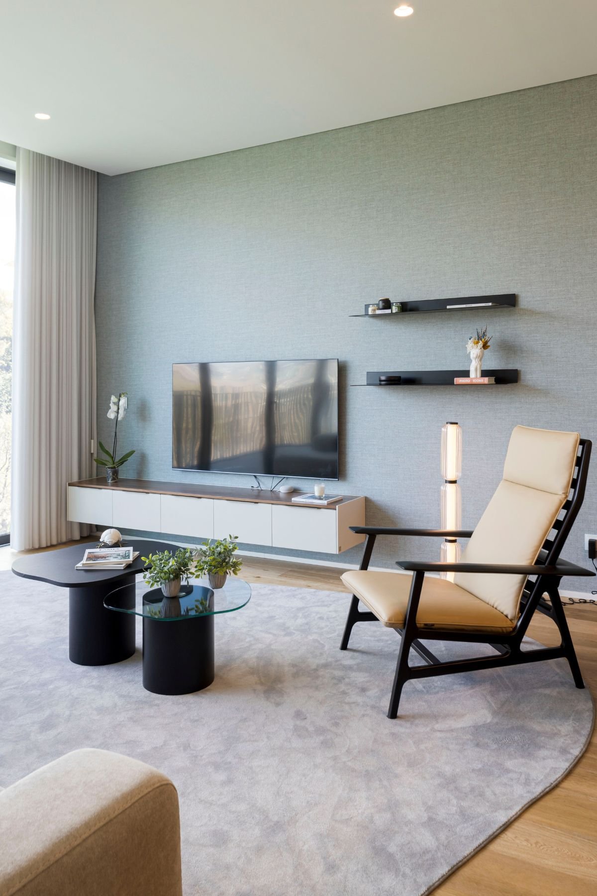 Sala de estar moderna com móvel de sala para TV, cadeirão, candeeiro de pé e mesas de centro sobre tapete cinza.