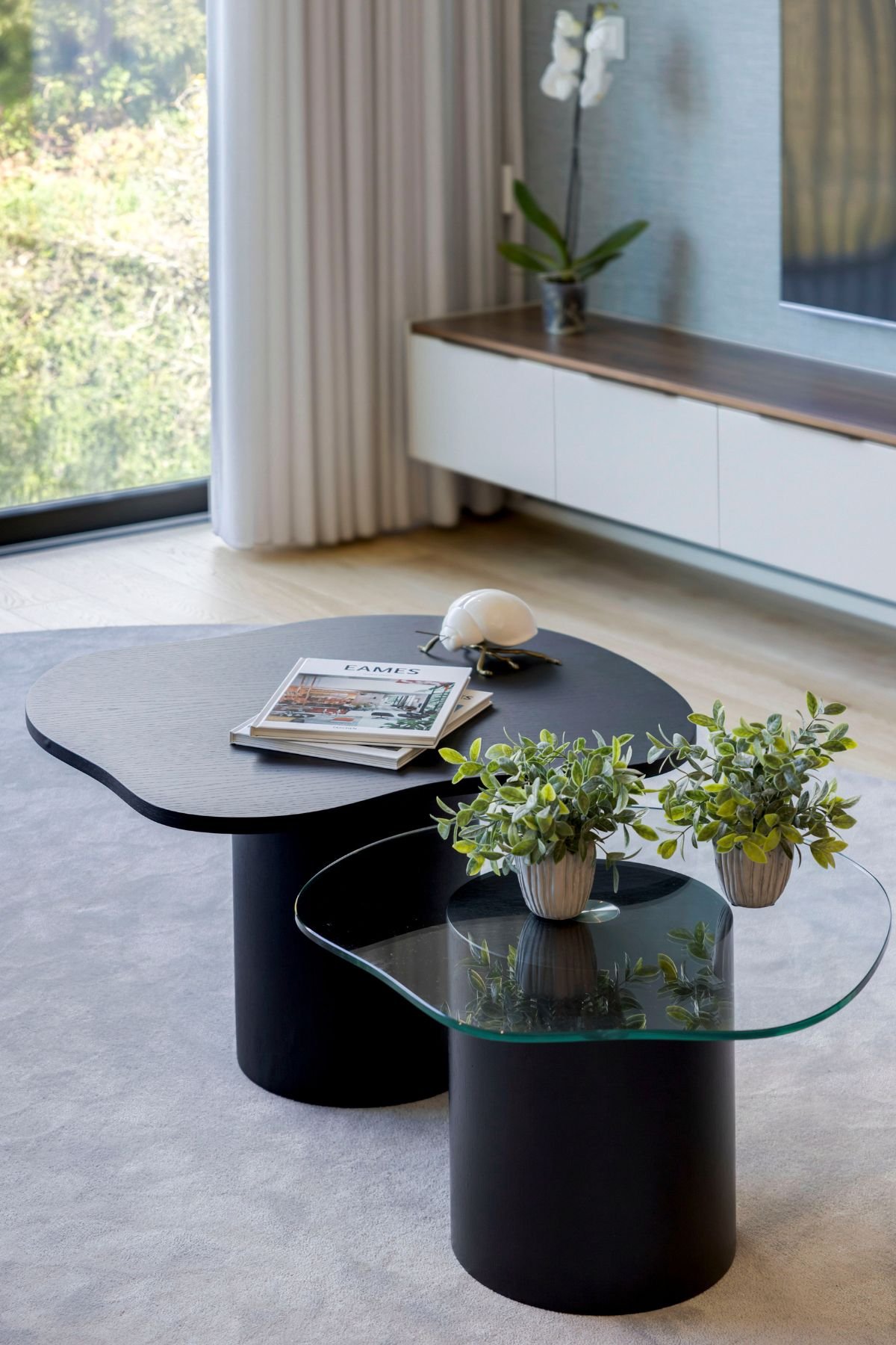 Conjunto de mesas de centro pretas numa sala de estar, com vasos decorativos e móvel de sala para TV ao fundo.