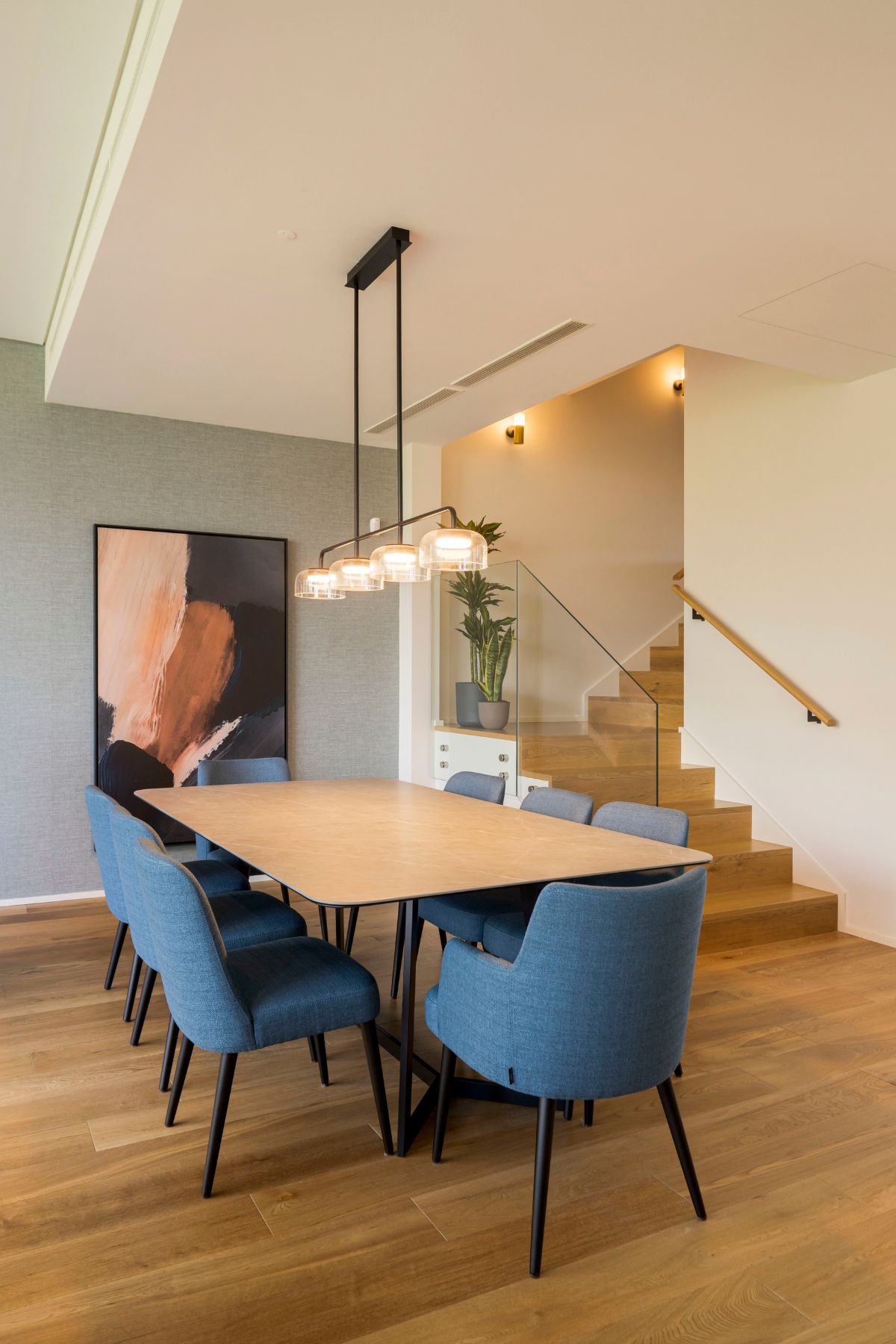 Sala de jantar elegante com mesa para sala de jantar, cadeira de jantar estofada a azul e escadas interiores ao fundo.