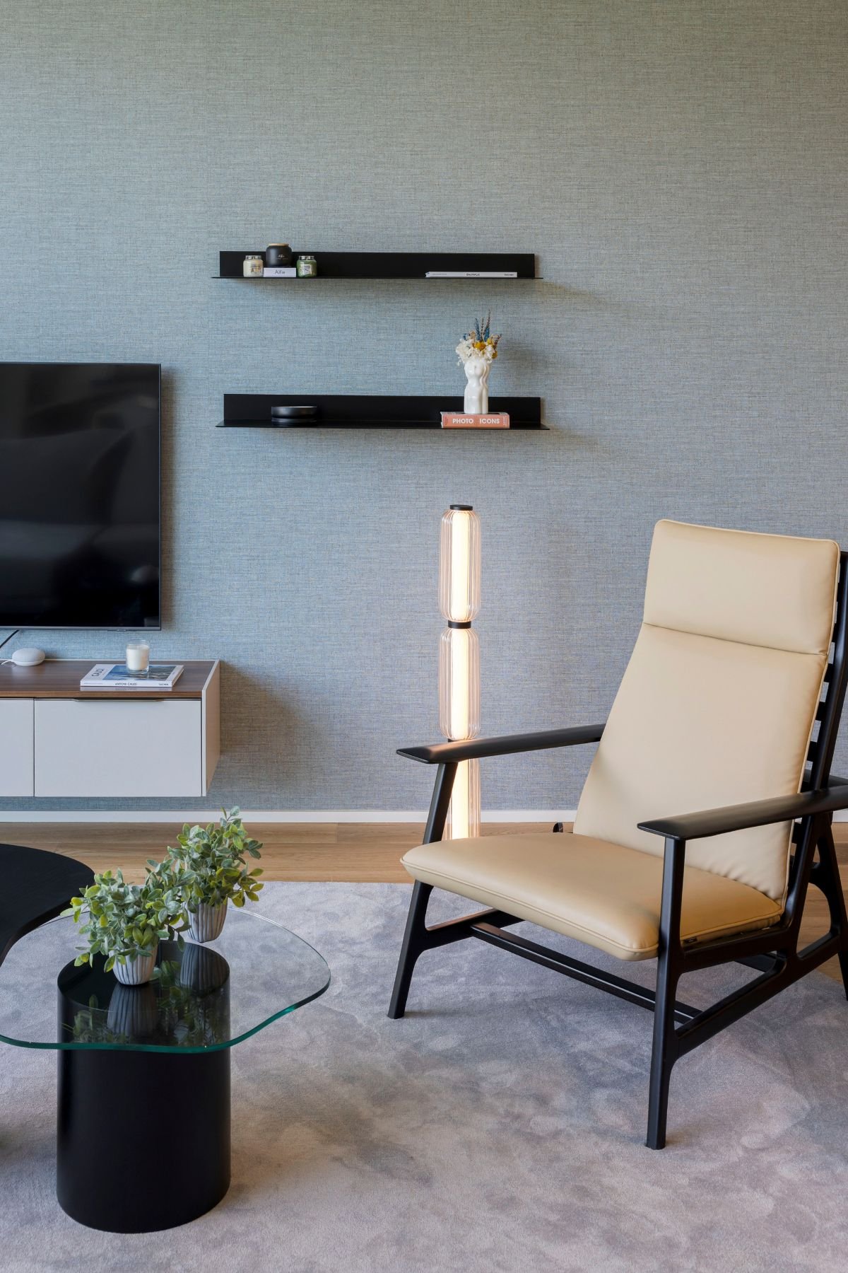 Cadeirão de leitura com candeeiro de pé, mesas de apoio decorativas e móvel de sala para TV numa sala de estar moderna.