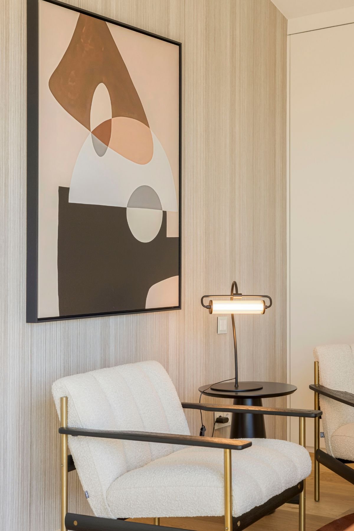 Recanto de reunião com cadeirão bouclé, mesa de apoio e candeeiro secretária, complementado por quadros decorativos na parede.