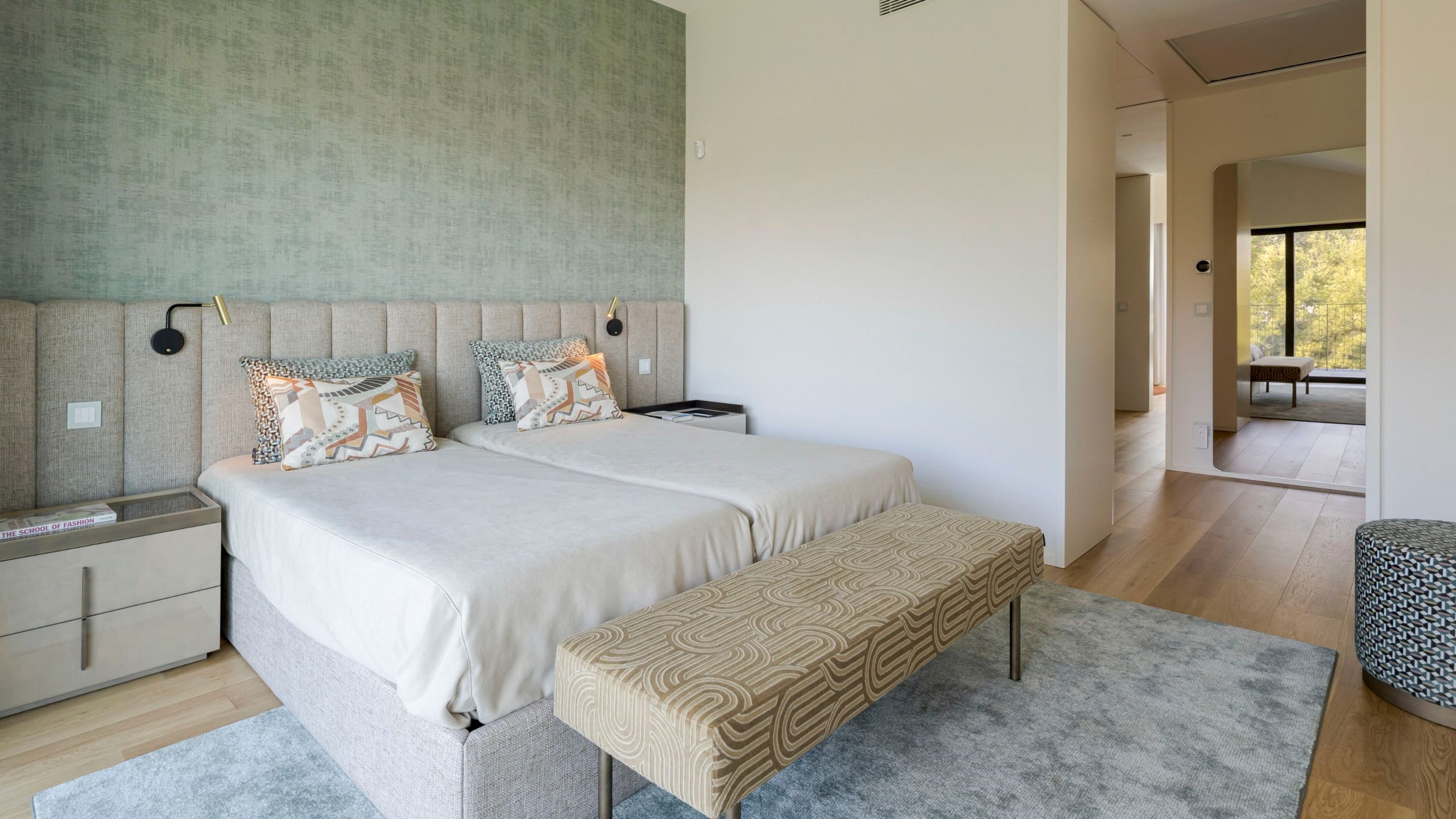 Cama de casal com cabeceira estofada, mesas de cabeceira modernas, móvel banqueta e tapete para quarto em tons neutros.