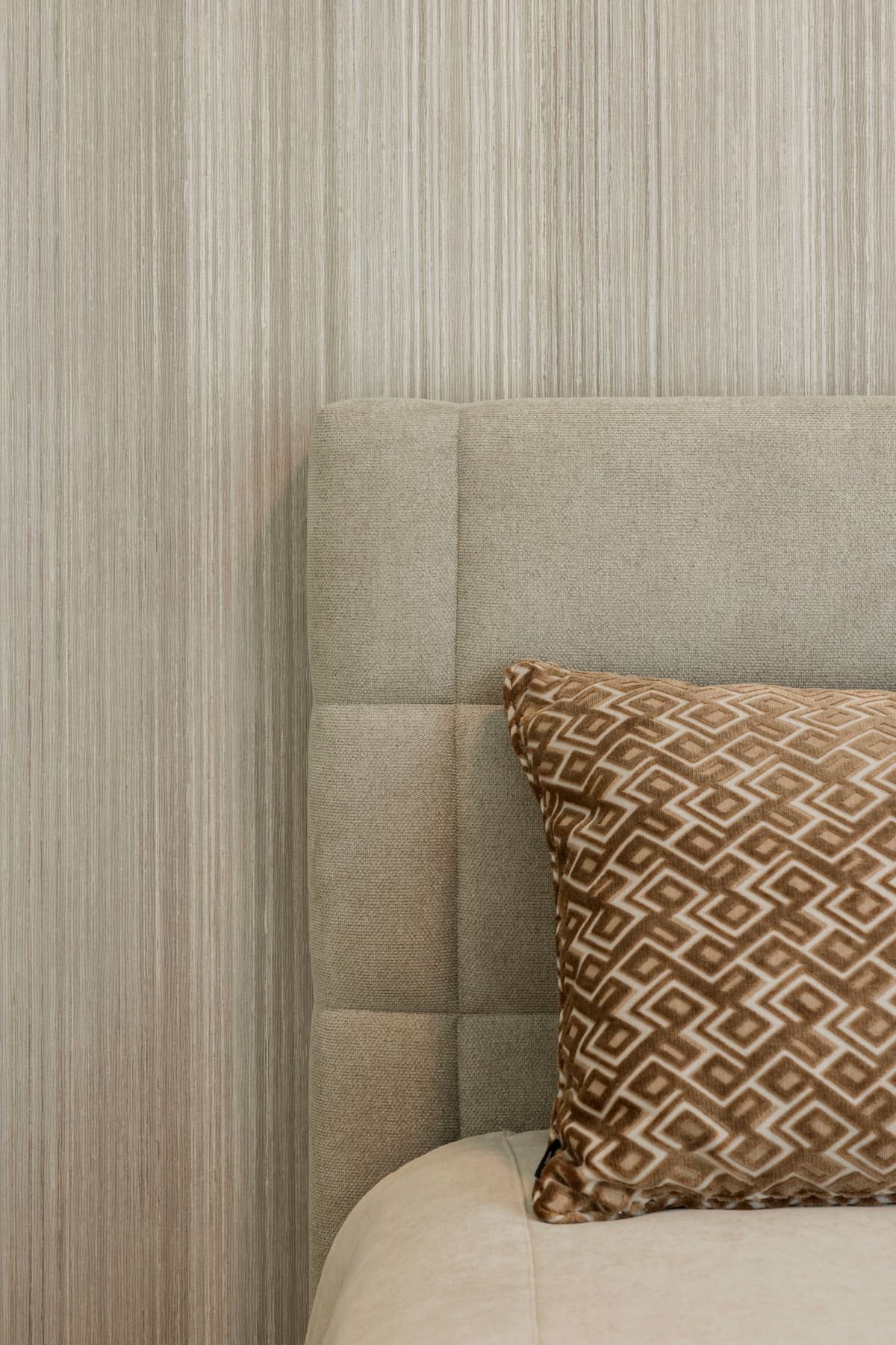 Detalhe da cabeceira de cama estofada com textura quadriculada suave e almofada com padrão geométrico.