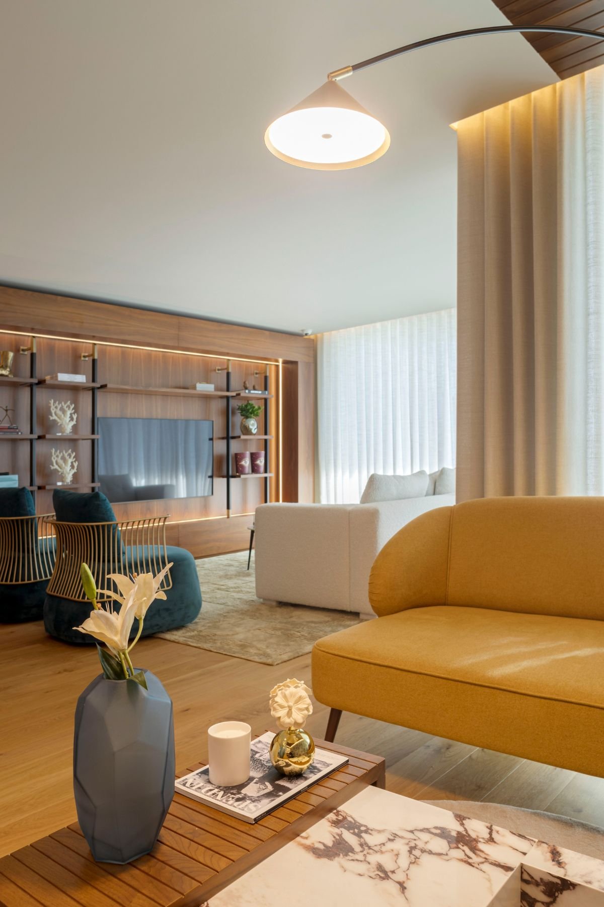 Pormenor do sofá amarelo torrado no lounge com vista de fundo para a sala de estar principal e candeeiro de pé curvo.