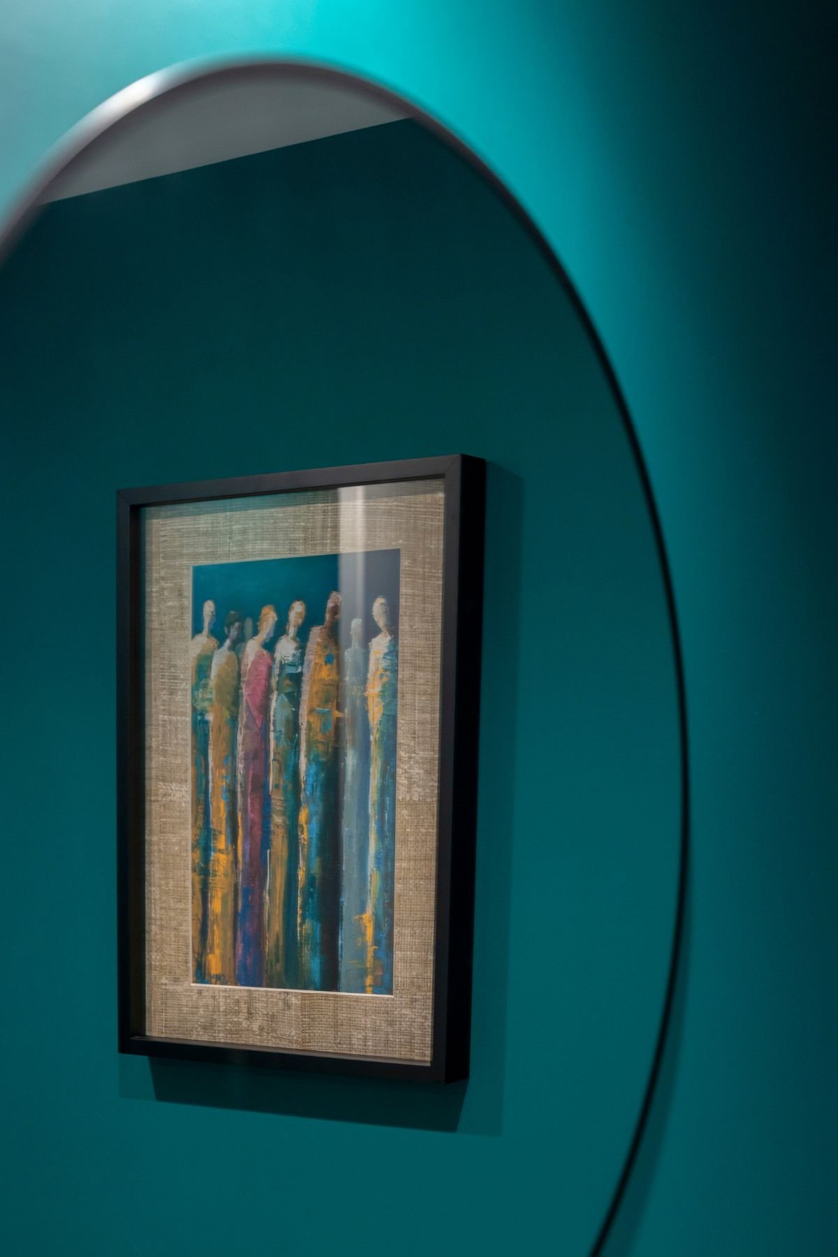 Pormenor do espelho redondo a refletir quadro com pintura abstrata sobre parede de tom azul-esmeralda.
