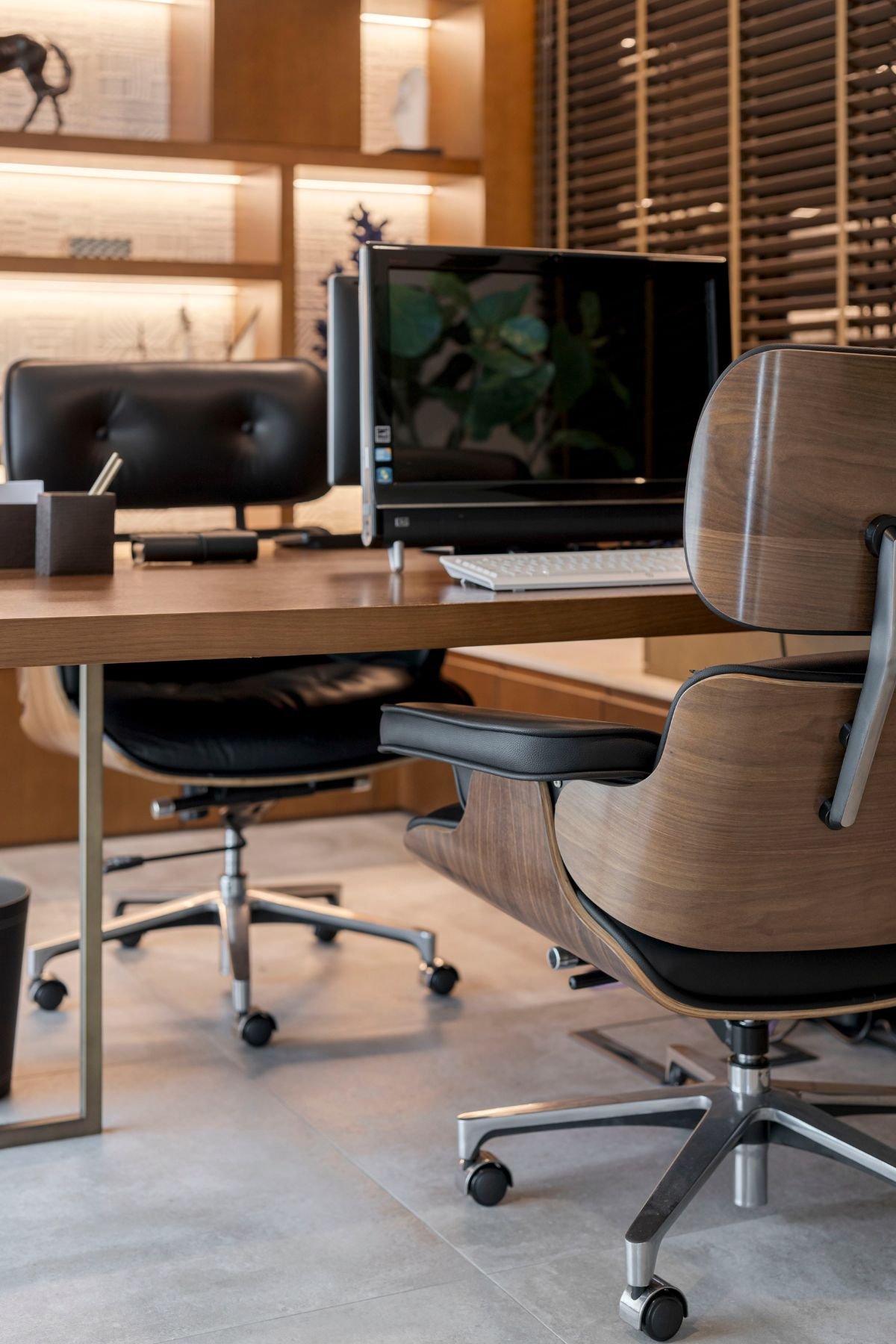 Pormenor da cadeira de escritório ergonómica com acabamento em madeira e estofo preto, em frente à secretária com monitor.