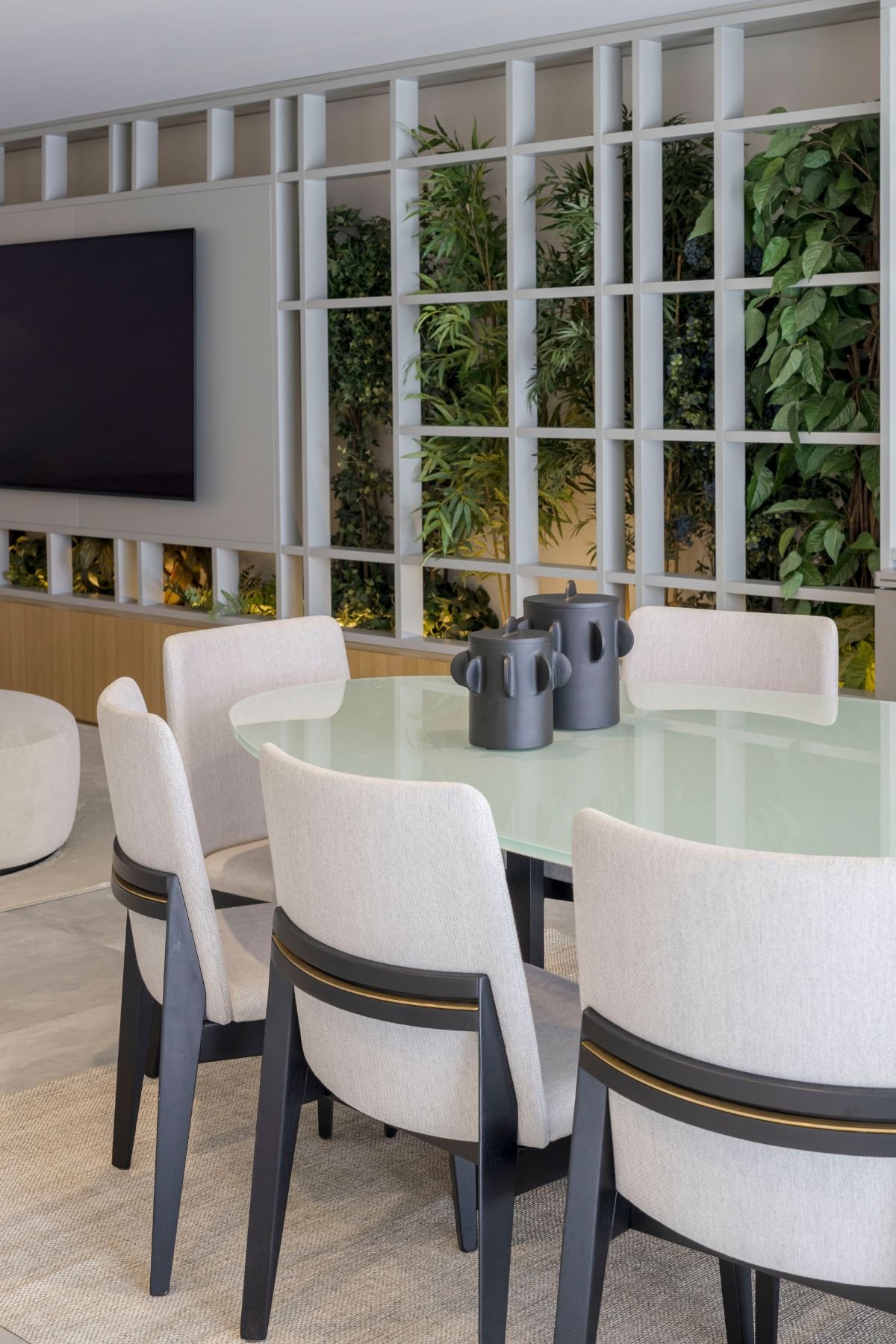 Pormenor da mesa da zona de jantar com peças decorativas pretas, com vista para as cadeiras estofadas e para o painel de plantas da sala de cinema.