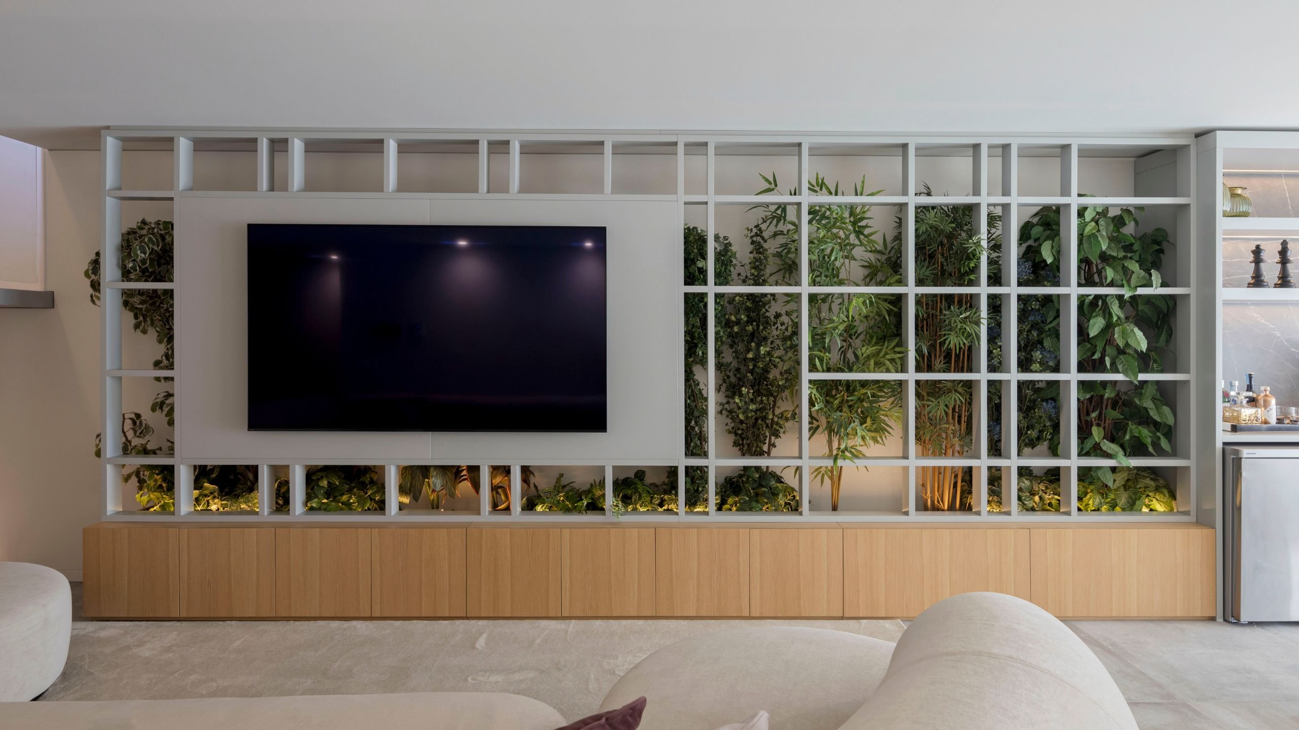 Móvel por medida da sala de cinema com ecrã de televisão encastrado, estrutura geométrica com jardim vertical e base em madeira com arrumação.